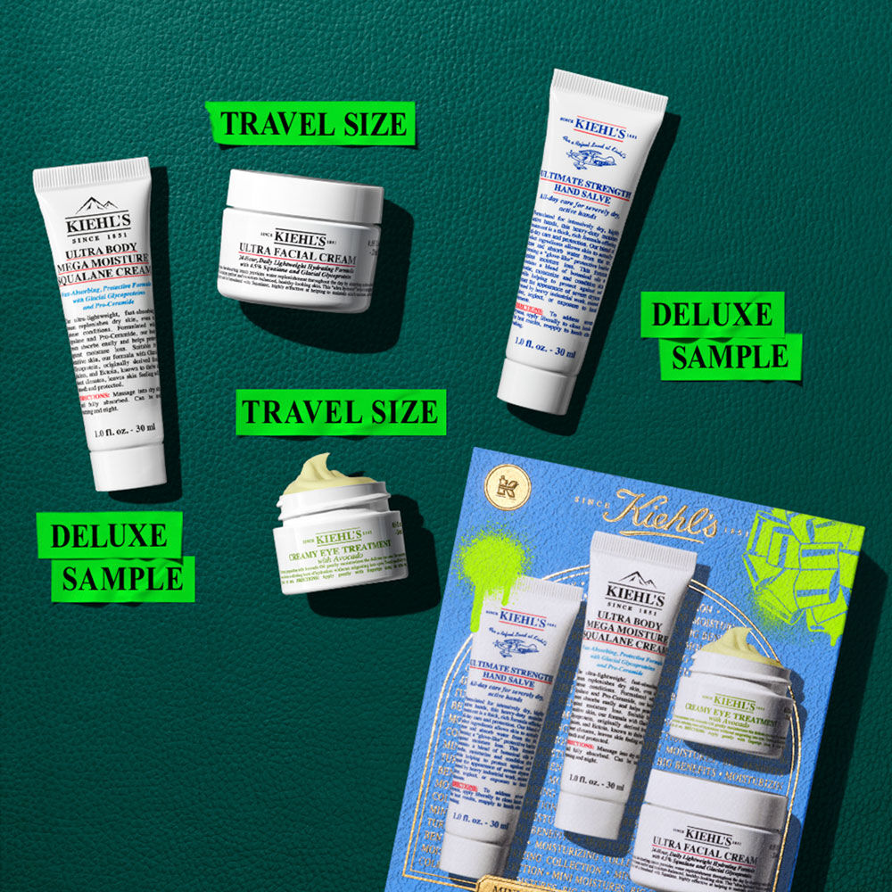 Grafico con cuatro productos Kiehl's blancos sobre fondo blanco. De izquierda a derecha: "ULTIMATE STRENGTH HAND SALVE", "ULTRA BODY MEGA MOISTURE SQUALANE CREAM", "CREAMY EYE TREATMENT WITH AVOCADO" (tarro pequeno con crema amarilla) y "ULTRA FACIAL CREAM" (tarro grande). Los tarros de crema de ojos y facial estan apilados.