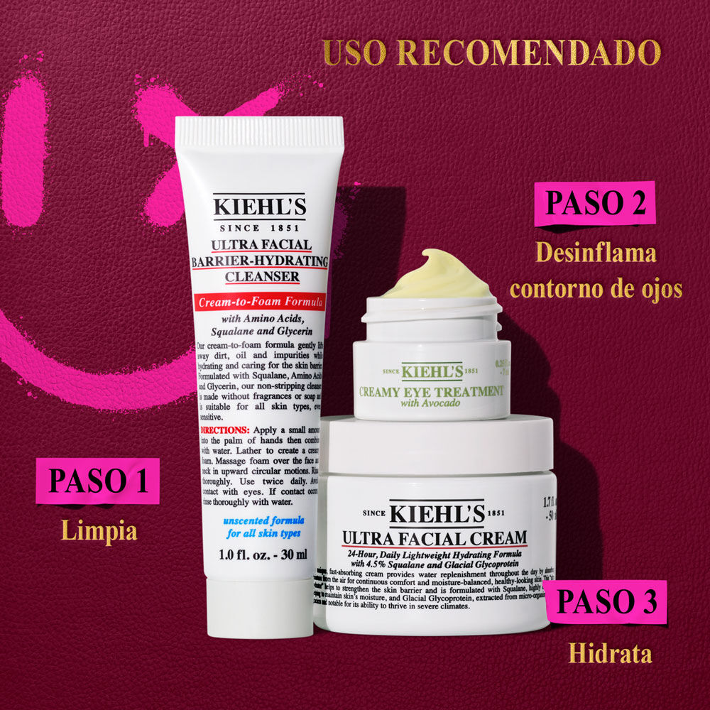 Un grafico sobre fondo rojo oscuro con acentos rosas, muestra "RECOMMENDED ORDER OF USE" arriba a la derecha. Debajo, tres productos Kiehl’s: a la izquierda, "KIEHL’S ULTRA FACIAL BARRIER-HYDRATING CLEANSER" (Paso 1: Limpieza profunda). Apilados a la derecha estan: un tarro pequeno de "KIEHL’S CREAMY EYE TREATMENT WITH AVOCADO".