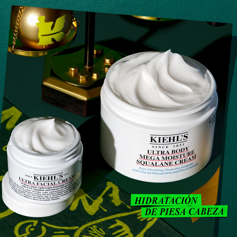 Un grafico sobre fondo verde oscuro con detalles dorados y verdes. Muestra dos tarros blancos abiertos con crema. El mas pequeno es "KIEHL’S ULTRA FACIAL CREAM", y el mas grande "KIEHL’S ULTRA BODY MEGA MOISTURE SQUALANE CREAM". Un adorno dorado con logo "K" verde. Texto verde: "Give the gift of HEAD-TO-TOE HYDRATION this holiday!".