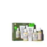 Un grafico muestra una caja de regalo Kiehl’s verde y dorada con cuatro productos. A la derecha, se ven la Crema de Corps, Acondicionador y Champu de Aminoacidos, y el Exfoliante Corporal de Pomelo. La caja dice "OH SO SOFT & SUDSY" abajo.