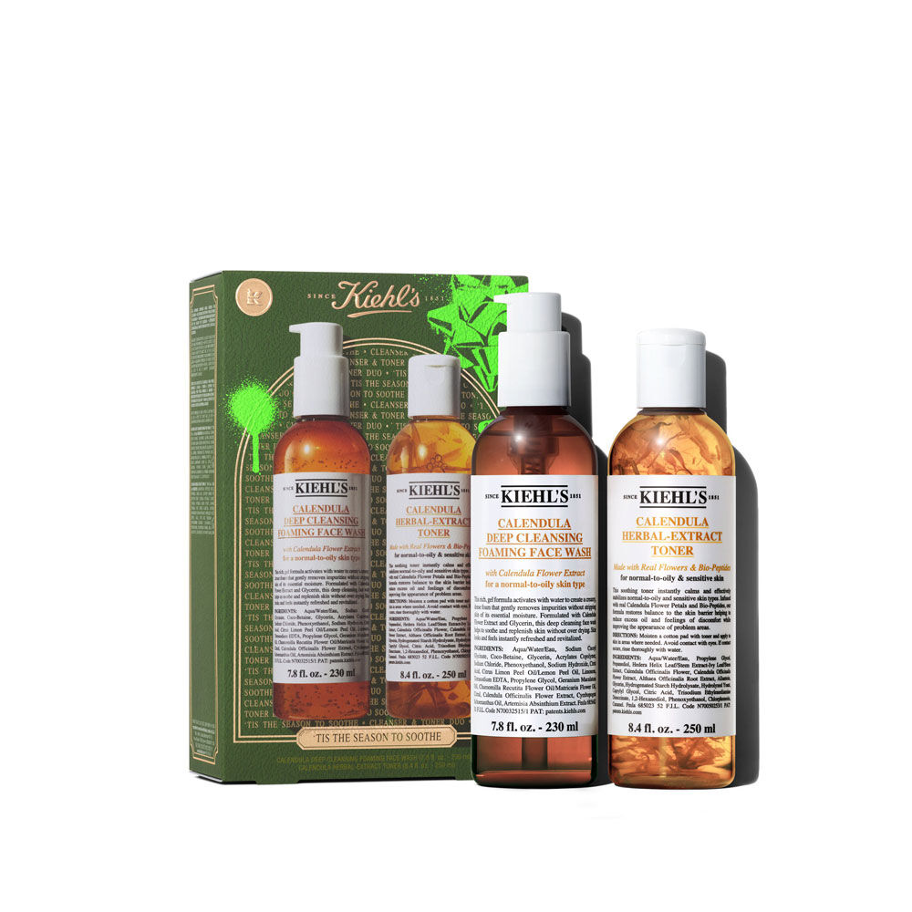 Un grafico muestra una caja de regalo Kiehl’s verde y dorada con dos botellas: "KIEHL'S CALENDULA DEEP CLEANSING FOAMING FACE WASH" y "KIEHL'S CALENDULA HERBAL-EXTRACT TONER". La caja tiene acentos verdes brillantes y la frase "TIS THE SEASON TO SOOTHE" abajo.